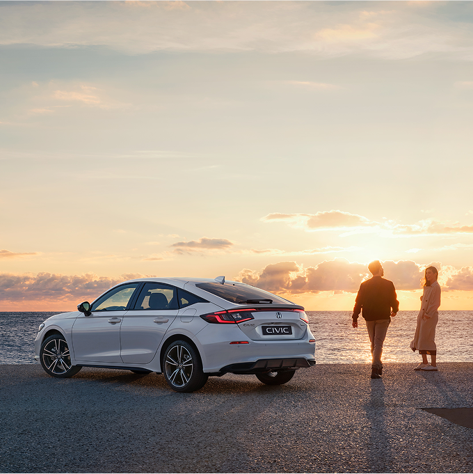 Honda Civic Hybrid geparkeerd naast een zee, mensen staan aan de rechterkant van de auto.